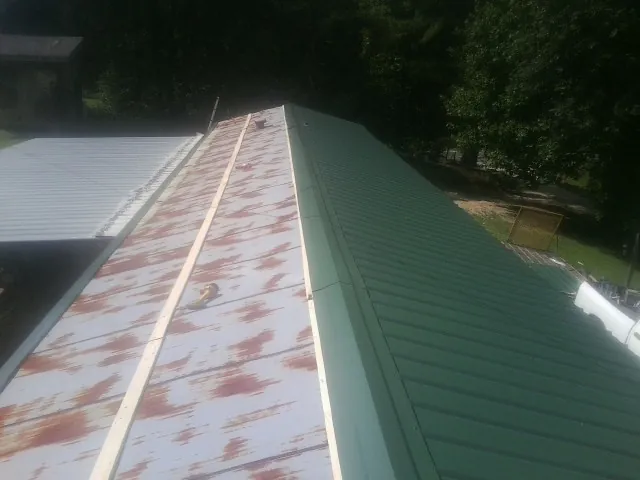 Old rusted panels beside newly installed green metal roofing — Wind Damage Roof Repair by Roofing Brothers in Newport