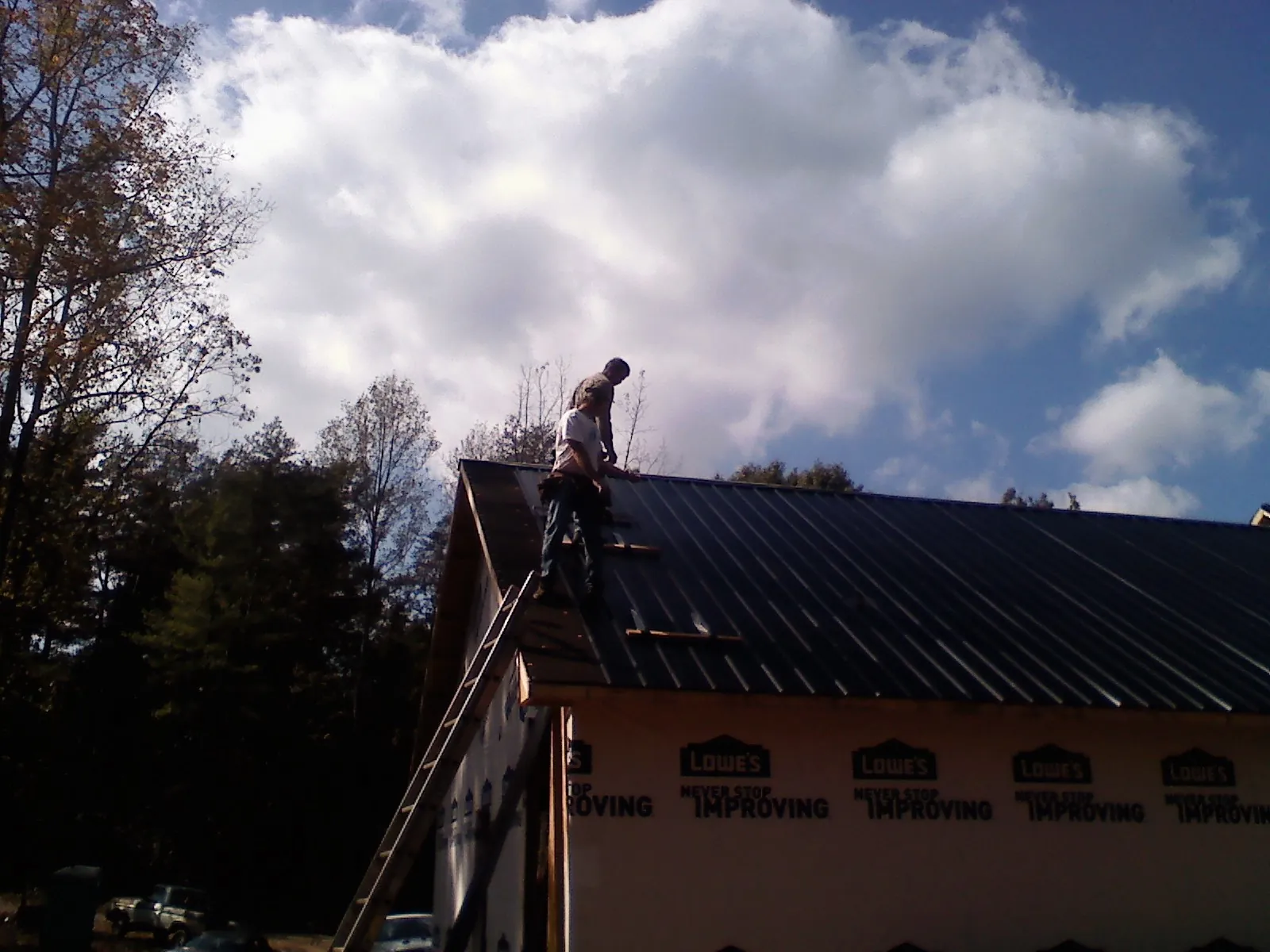 Roofer fastening dark metal panels high against a cloudy sky, from a Roof Inspection job in Newport