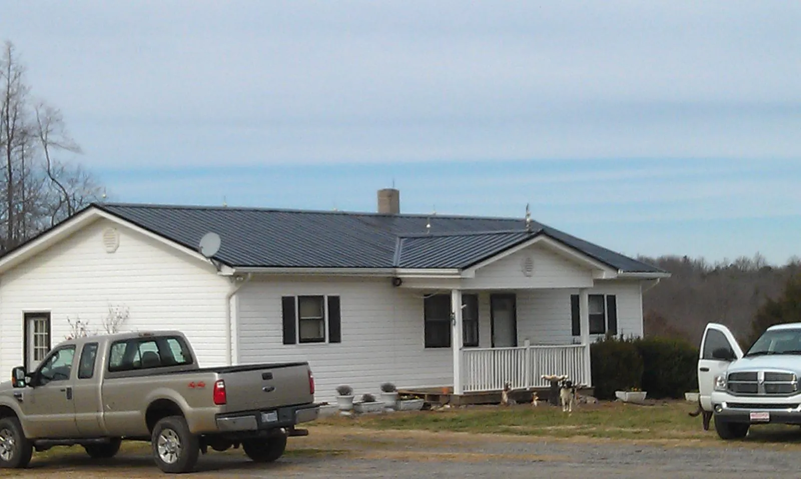 Finished dark metal roof on a white ranch home with work trucks parked in Newport